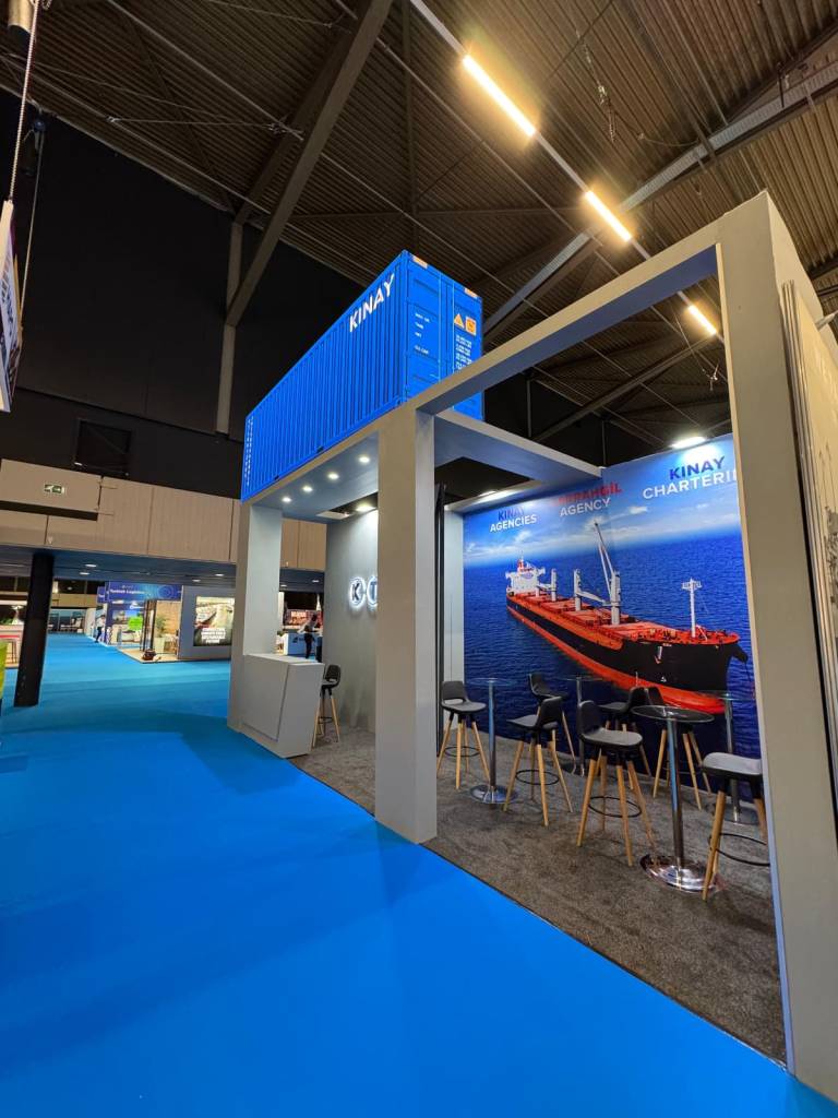 KINAY branded breakbulk exhibition stand with illuminated façade and container-inspired visual identity, Industrial brand-focused exhibition booth featuring global route graphics and maritime identity for breakbulk audiences
